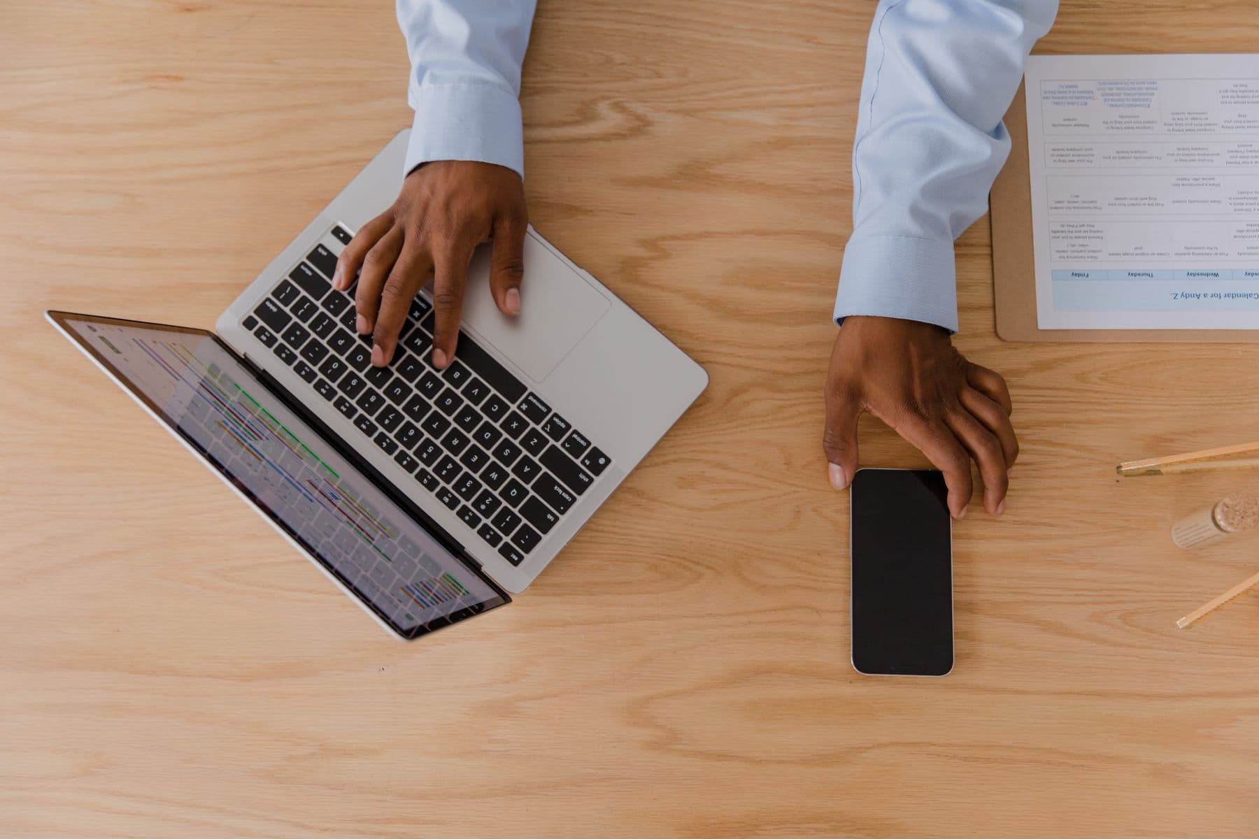 An overhead view of hands working with a laptop, phone, and printed schedule.